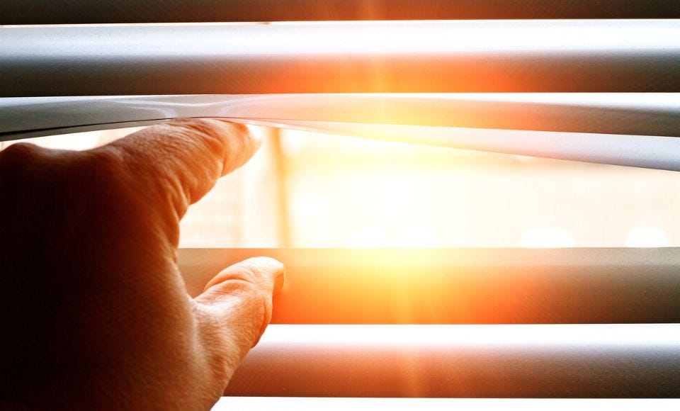Eine Hand öffnet die Rollos einen Spalt Sonne scheint durch