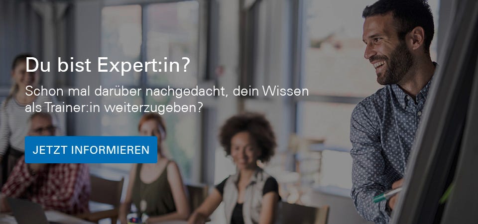 Trainer steht vor dem White Board und lacht. Im Hintergrund sind Schüler zu sehen.