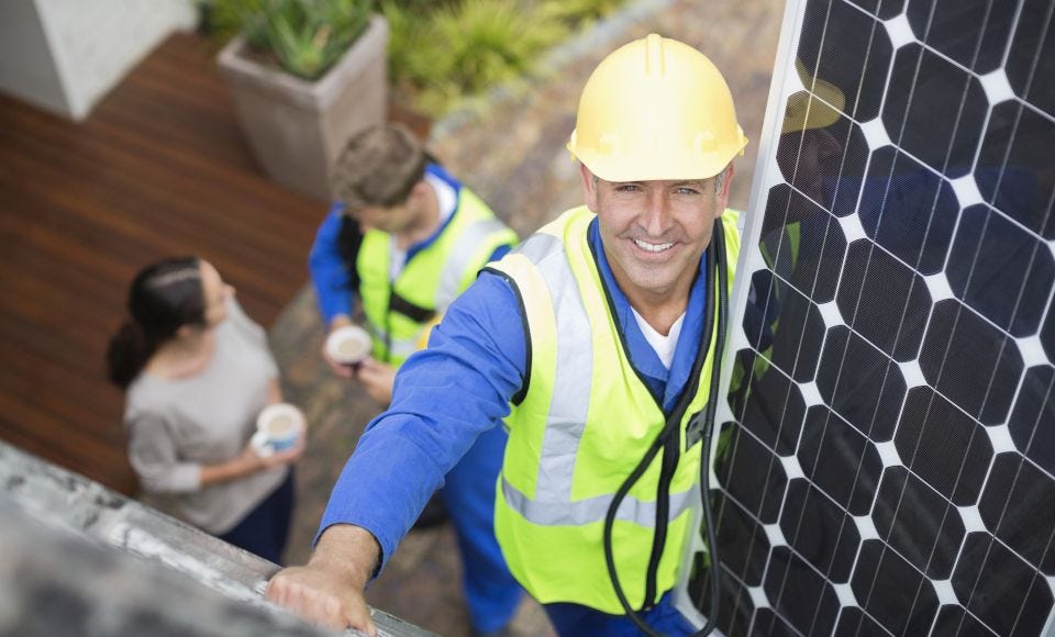 Handwerker trägt ein PV-Modul auf das Dach eines Hauses