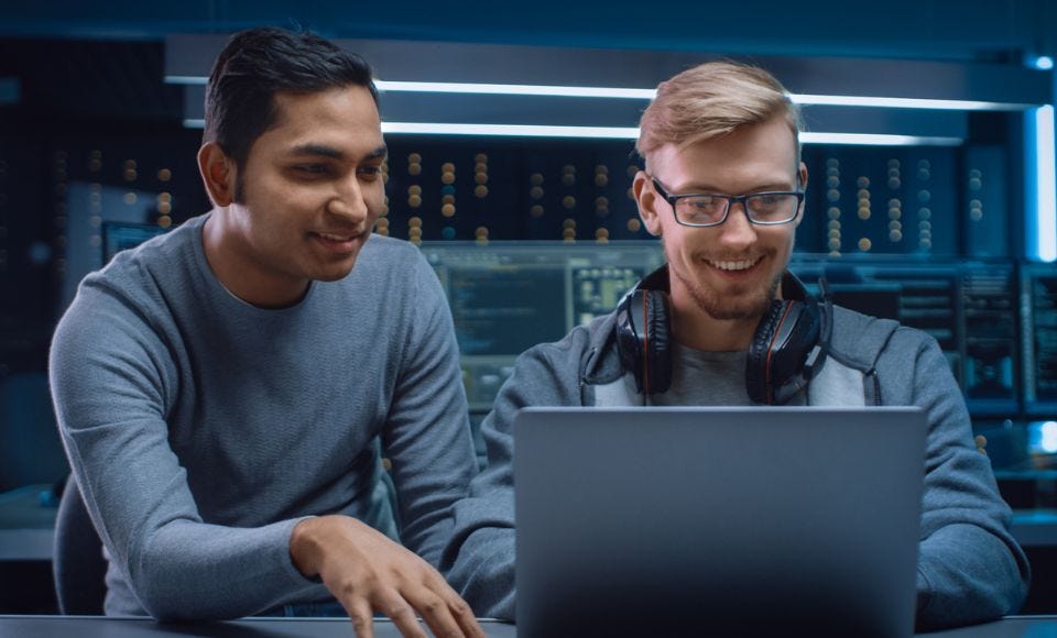 Zwei Männer vor einem Laptop die lächeln und gemeinsam tippen