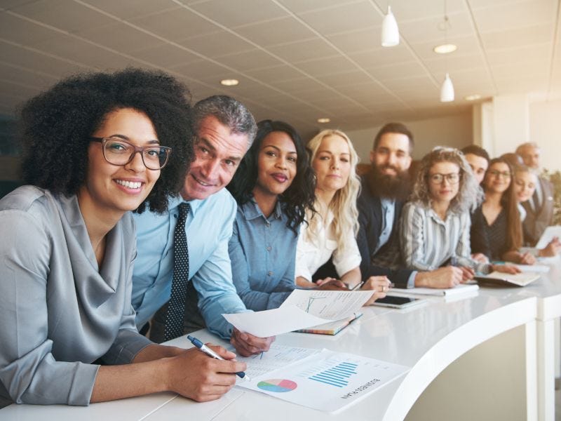 Gesch&auml;ftsleute an einem gebogenen Tisch pr&uuml;fen Diagramme und Dokumente, um Gesch&auml;ftszahlen und Strategien zu besprechen.