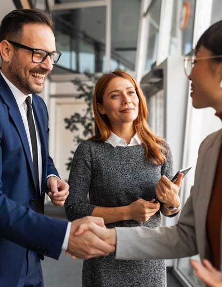 Mehrere Personen begrüßen sich per Handschlag in einem modernen Büro. Weitere Teilnehmende stehen daneben und verfolgen das Gespräch in professioneller Atmosphäre.