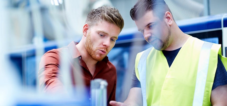 Auditor und Produktionsmitarbeiter sichten technische Unterlagen an der Maschine.