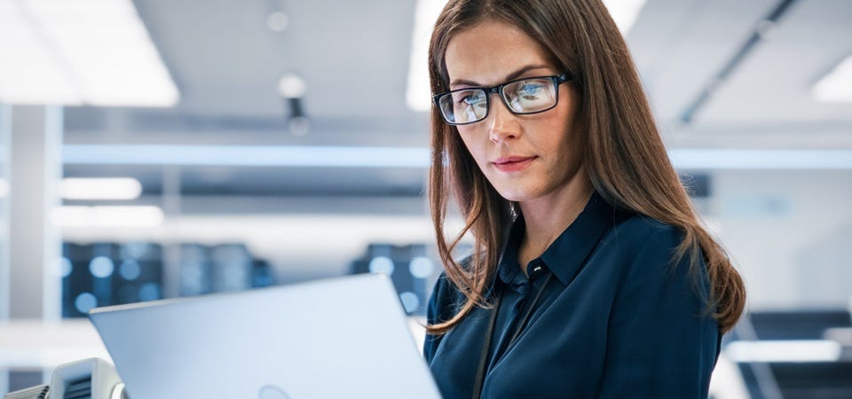 Frau mit Brille arbeitet konzentriert am Laptop in heller, technisch ausgestatteter Arbeitsumgebung.