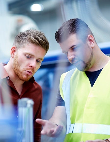 Auditor und Produktionsmitarbeiter sichten technische Unterlagen an der Maschine.