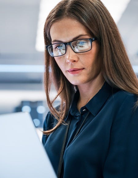 Frau mit Brille arbeitet konzentriert am Laptop in heller, technisch ausgestatteter Arbeitsumgebung.