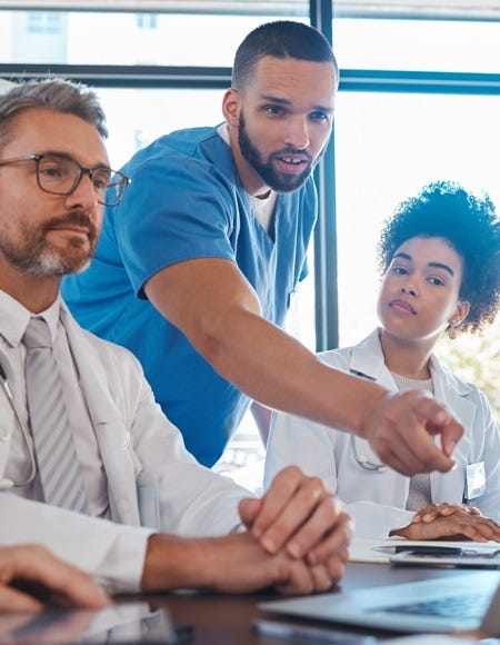 Ärzteteam in einer QM-Besprechung: Ein Mediziner zeigt auf den Laptopbildschirm, während Kolleginnen und Kollegen aufmerksam zuhören.