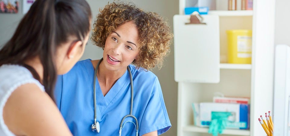 Ärztin im Gespräch mit Patientin in Praxisraum, hört aufmerksam zu und erklärt freundlich medizinische Informationen.