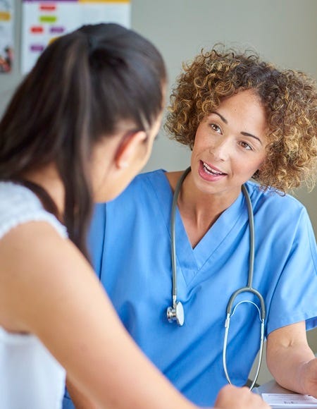 Ärztin im Gespräch mit Patientin in Praxisraum, hört aufmerksam zu und erklärt freundlich medizinische Informationen.