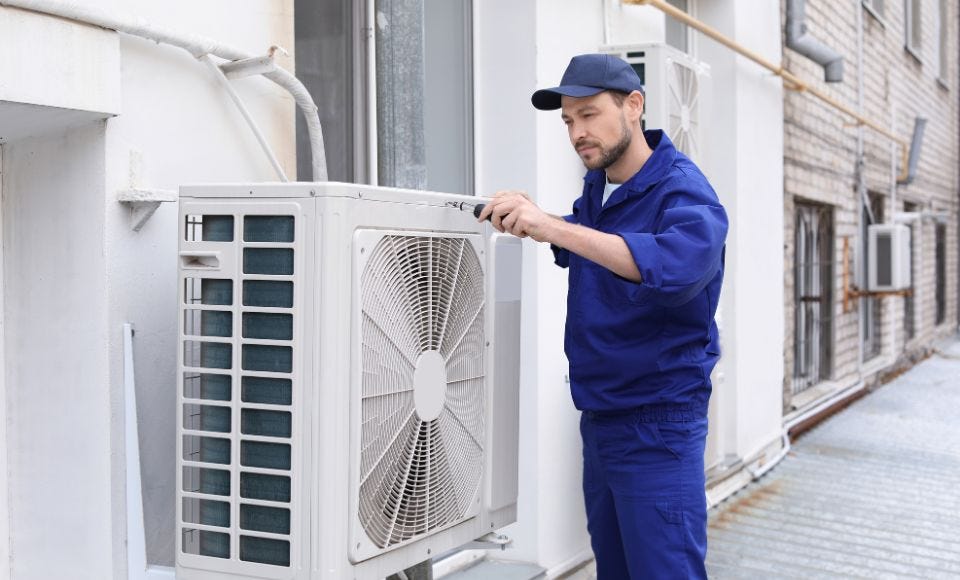 Mann prüft eine Wärmepumpe, an der Außenwand eines Hauses