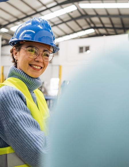 Mitarbeiterin mit Schutzhelm und Warnweste im Gespr&auml;ch auf einem Industriegel&auml;nde.