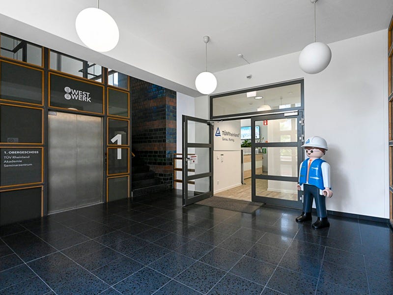 T&Uuml;V Playmobil Mann begr&uuml;&szlig;t am Eingangsportal