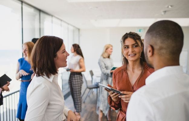 Drei junge Menschen netzwerken auf einer Veranstaltung in einem Konferenzraum.