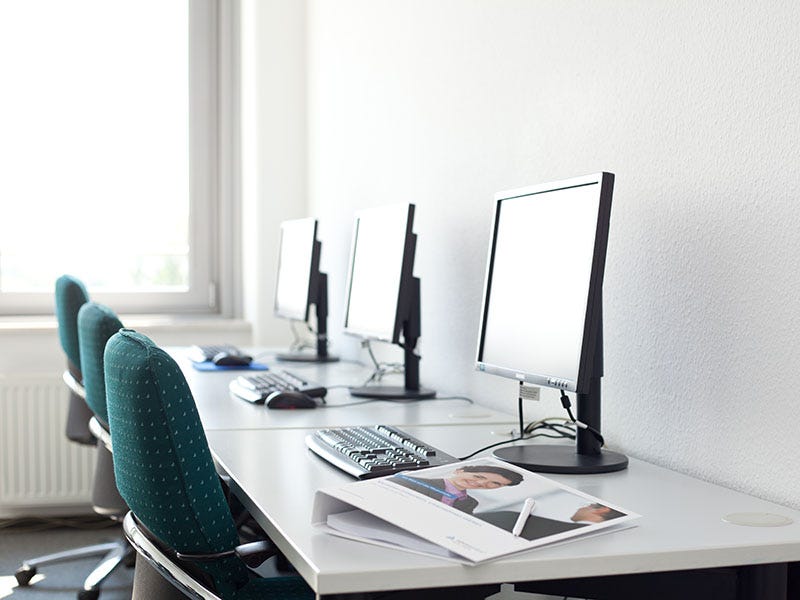 Drei Arbeitsplätze mit IT-Ausstattung. Die Tische sind an die Wand gestellt und bieten mit jeweils einem Bildschirm, Maus, Tastatur und Willkommensmappe eine angenehme Arbeitsatmospähre. 