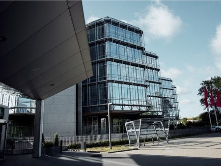 Außenansicht Seminarzentrum Hannover Außenansicht eines modernen, mehrgeschossigen Bürogebäudes mit markanter Glasfassade und gestufter Architektur unter blauem Himmel, mit Fahrradständern.