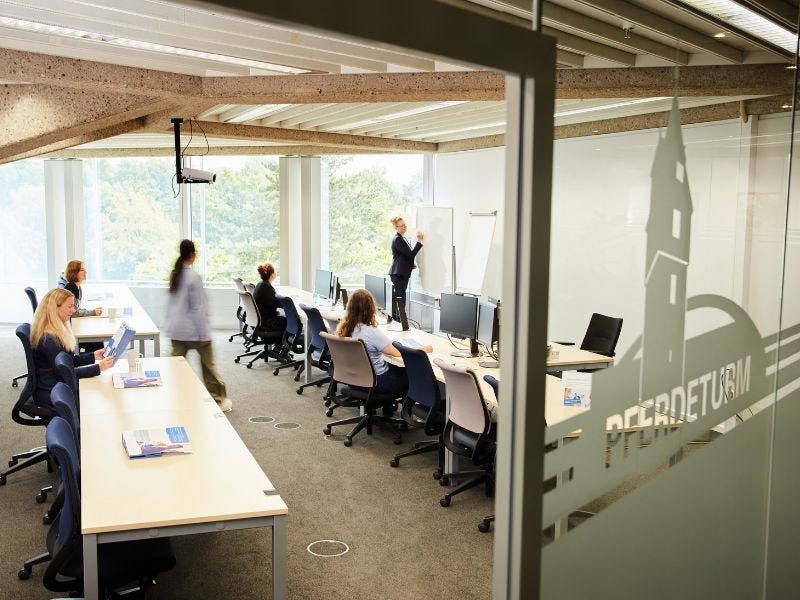 Blick in einen hellen Seminarraum mit modernen, ergonomischen St&uuml;hlen. Im Hintergrund sind Fenster mit Blick ins Gr&uuml;ne. Auf der Glast&uuml;r steht der Raumname "Pferdeturm".