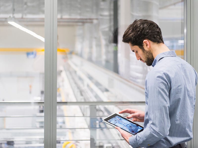 Unsere Weiterbildungen in Hannover vermitteln Elektrotechnik-Fachkenntnisse Ein Mann mit Computer-Tablet steht auf der Balustrade einer Fertigungshalle