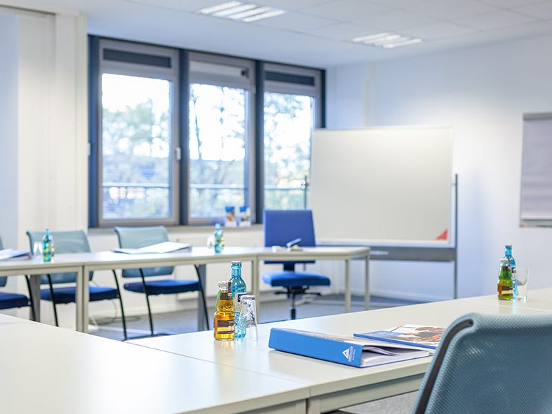 Ein Schulungsraum mit Fenstern, Flipchart und Getränken auf den Tischen.