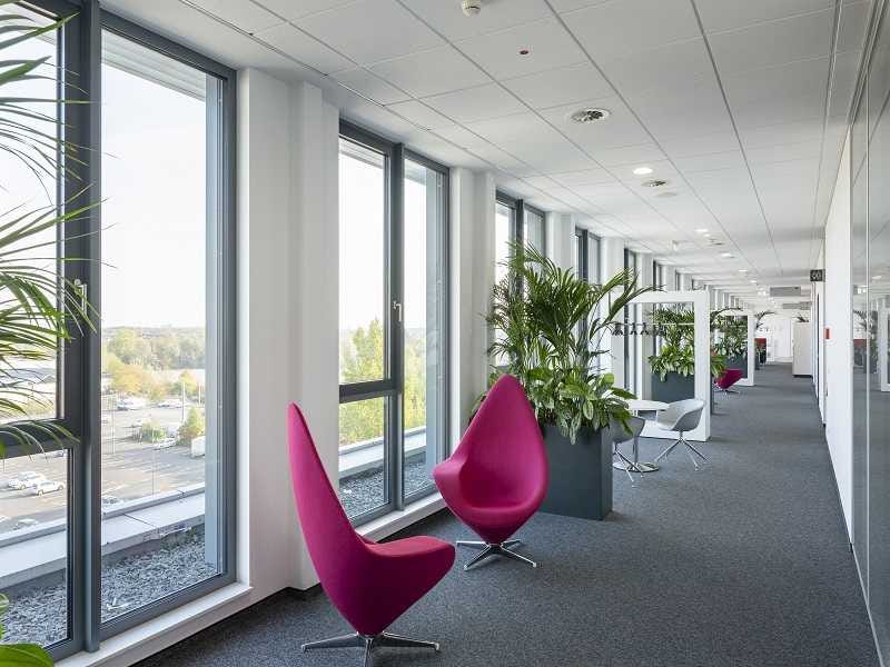 Heller Lounge-Bereich mit modernen pinken Sesseln, gro&szlig;en Fensterfronten und gr&uuml;nen Pflanzen als Raumteiler.