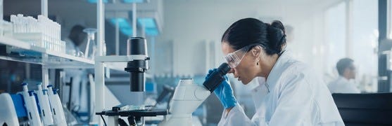 eine Dame arbeitend im Labor mit Blick durch ein Mikroskop