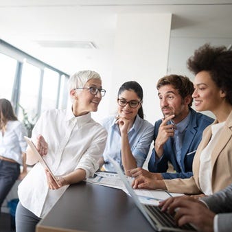 Mehrere Berufstätige in einem modernen Büro tauschen sich in lockerer Atmosphäre aus, während eine Frau mit Tablet etwas präsentiert.