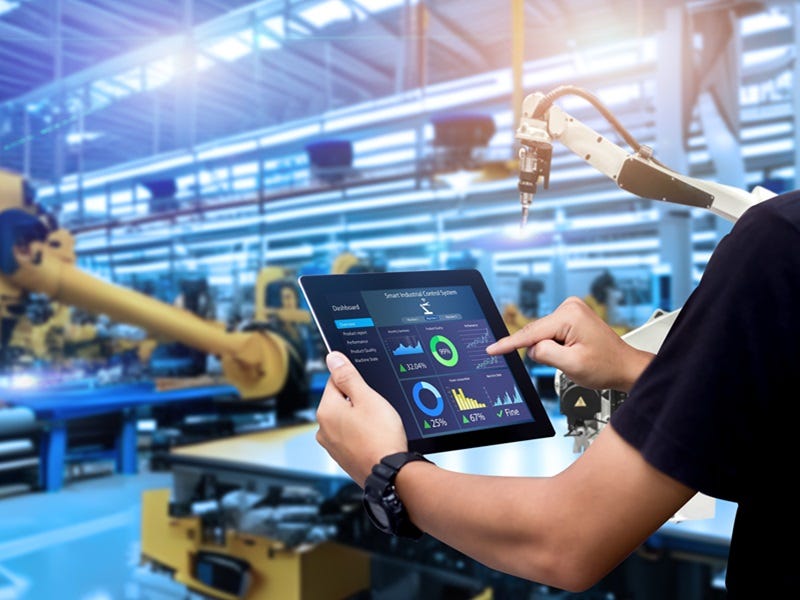 Digitale Fabriksteuerung in der Industrie 4.0: Eine Person bedient ein Tablet mit einem Dashboard zur Überwachung von Produktionsprozessen, während im Hintergrund Industrieroboter in einer modernen, automatisierten Fertigungshalle arbeiten.