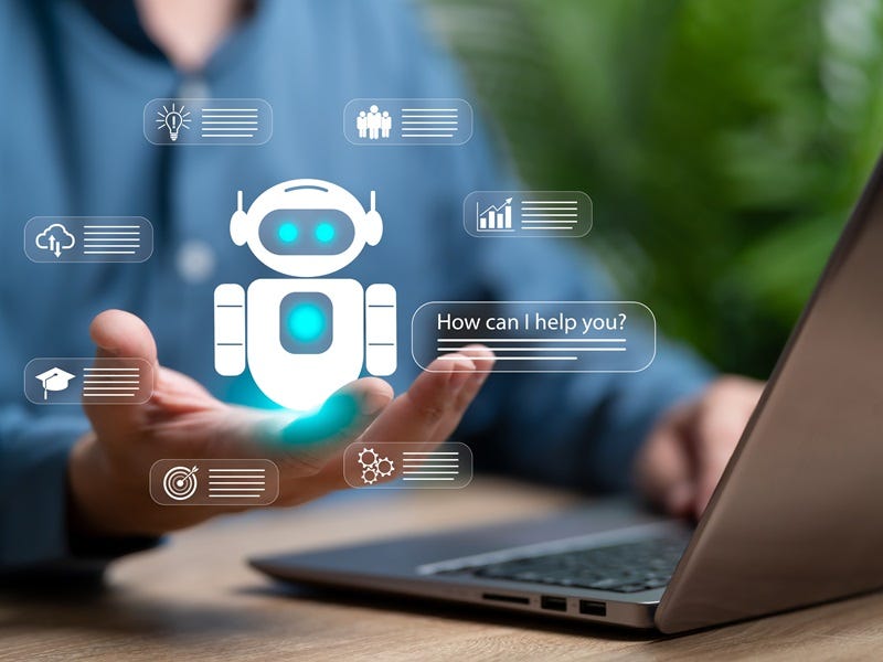 Eine Person sitzt an einem Schreibtisch vor einem Laptop und hält eine Hand leicht geöffnet in Richtung des Bildschirms. Über der Hand ist eine digitale Grafik eines Roboters mit Chat-Symbolen und Daten-Icons eingeblendet.