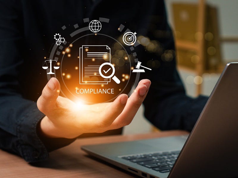 Symbolische Darstellung von Compliance und rechtlicher Sicherheit: Eine Hand hält eine leuchtende digitale Darstellung von Vorschriften, Gesetzessymbolen und Kontrollmechanismen, während im Hintergrund ein Laptop für die digitale Umsetzung steht.