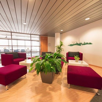 Lounge mit modularen roten Sitzm&ouml;beln um wei&szlig;e Tische, Topfpflanze und gr&uuml;ne Skyline-Grafik von Stuttgart an der Wand