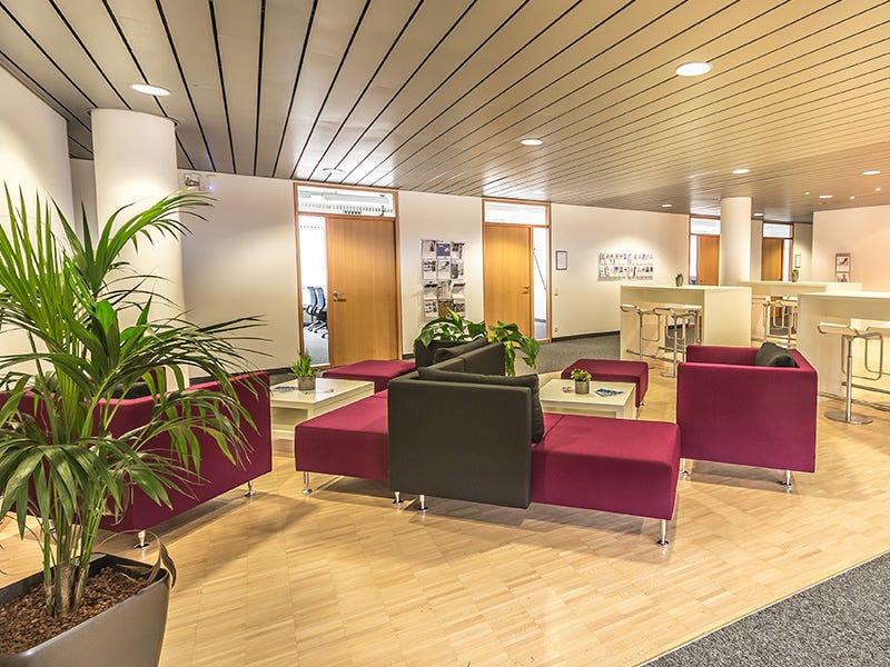 Das Bild zeigt einen modernen und eleganten Pausenbereich. Der Raum ist mit stilvollen Polstermöbeln in einer Mischung aus roter und schwarzer Farbe ausgestattet. Mehrere moderne Sessel und Sofas sind um niedrige Glastische gruppiert. 