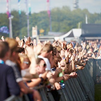 Große Menschenmenge bei einem Open-Air-Event, mit erhobenen Händen hinter einer Absperrung.