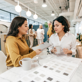 Zwei Frauen sitzen im großraumbüro und besprechen Dokumente bei einer Tasse Kaffee.
