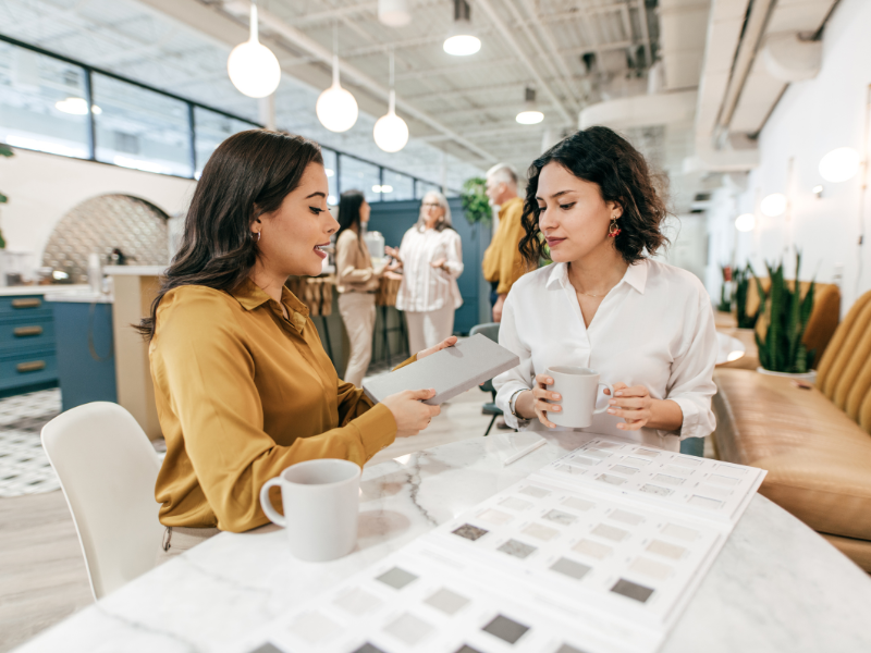 Zwei Frauen sitzen im großraumbüro und besprechen Dokumente bei einer Tasse Kaffee.
