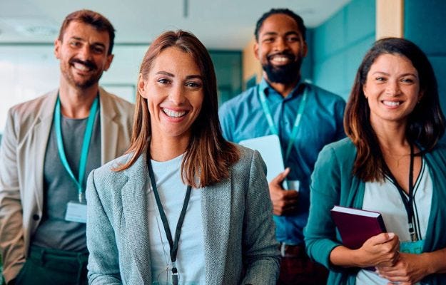 Zwei Frauen und zwei M&auml;nner mit Arbeitsmaterialien lachen freundlich in die Kamera