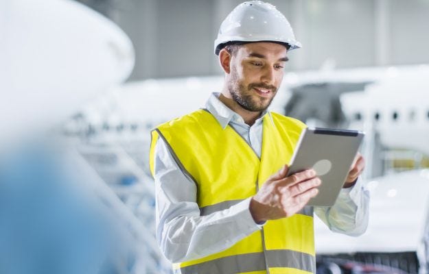 Arbeiter mit Helm und Schutzweste am Tablet