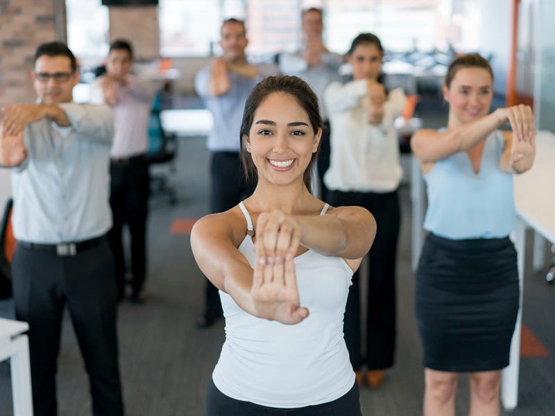 Betriebliche Gesundheitsförderung Seminare Eine Personengruppe macht Dehnungsübungen im Büro.