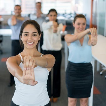 Betriebliche Gesundheitsförderung Seminare Eine Personengruppe macht Dehnungsübungen im Büro.