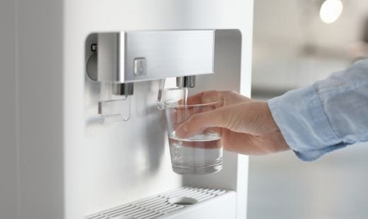 Hand hält ein Glas und holt Wasser vom Automaten