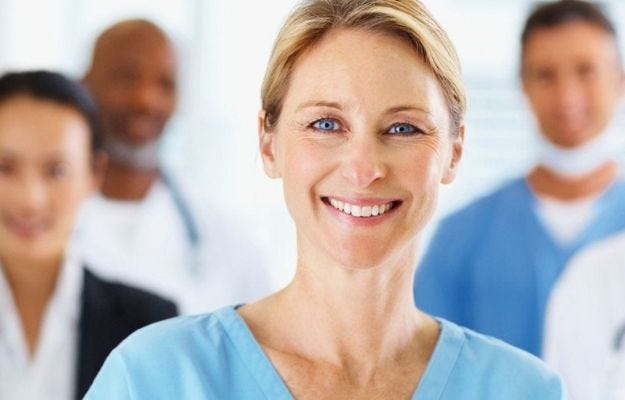 &Auml;rztin lacht freundlich in die Kamera im Hintergrund unscharf weitere Kollegen