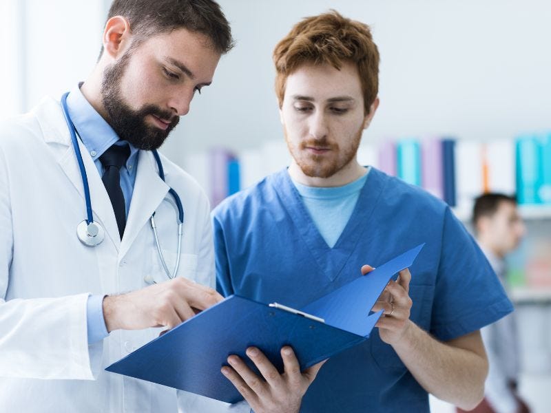 Ein Arzt und ein Pfleger stehen nebeneinander und gucken in eine Patientenakte.