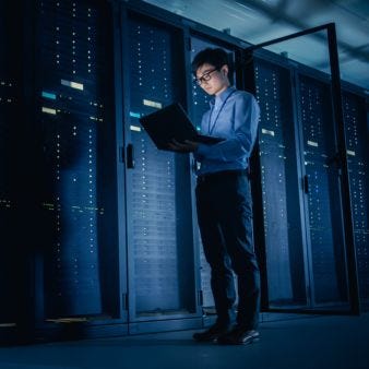 Ein Mann steht in einem Serverraum mit einem geöffneten laptop in der Hand