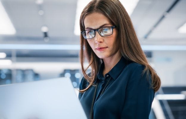 Eine Frau mit Brille und braunen Haaren schaut auf ein Notebook das im Vordergrund unscharf abgebildet ist