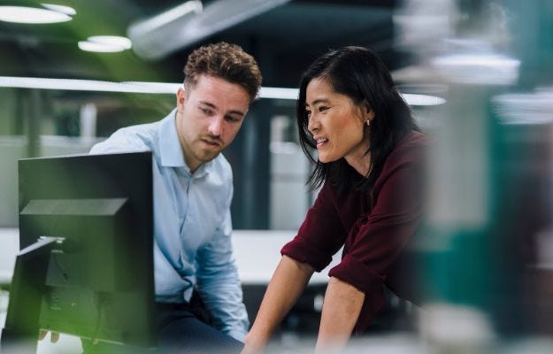 Managerin und Mitarbeiter stehen gemeinsam vor einem Bildschirm und beraten sich