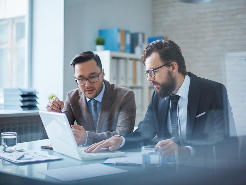 Zwei Gesch&auml;ftsleute besprechen in einem hellen B&uuml;ro gemeinsam Unterlagen und arbeiten an einem Laptop &ndash; Motiv zum 15. T&Uuml;V-Praxisforum Qualit&auml;t in K&ouml;ln.