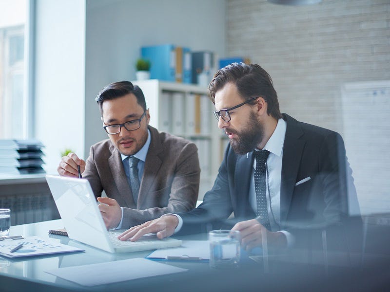 Mann mit Anzug sitzt vor einem aufgeklappten Laptop