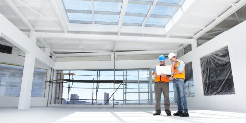 Zwei Bauplaner mit Sicherheitshelmen und Westen stehen auf einer Baustelle