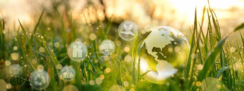 Transparenter Globus aus Glas im Sonnenlicht auf einer Wiese liegend, umgeben von Symbolen f&uuml;r Nachhaltigkeit, Energie und Umwelt