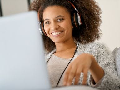 L&auml;chelnde Frau mit Headset sitzt vor einem Laptop und nimmt an einem Online-Webinar teil.