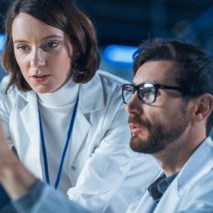 Frau und Mann in weißen Kitteln arbeiten gemeinsam an einem Schreibtisch